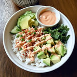 Un bowl de arroz con aguacate y salsa sobre una mesa de madera.