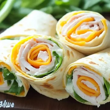 Three rolled tortilla wraps filled with turkey, cheese, and greens are arranged on a wooden surface.